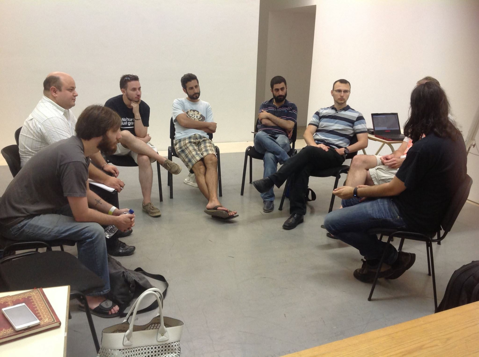 Participants seated in a circle listening to one another, a laptop on a table behind them